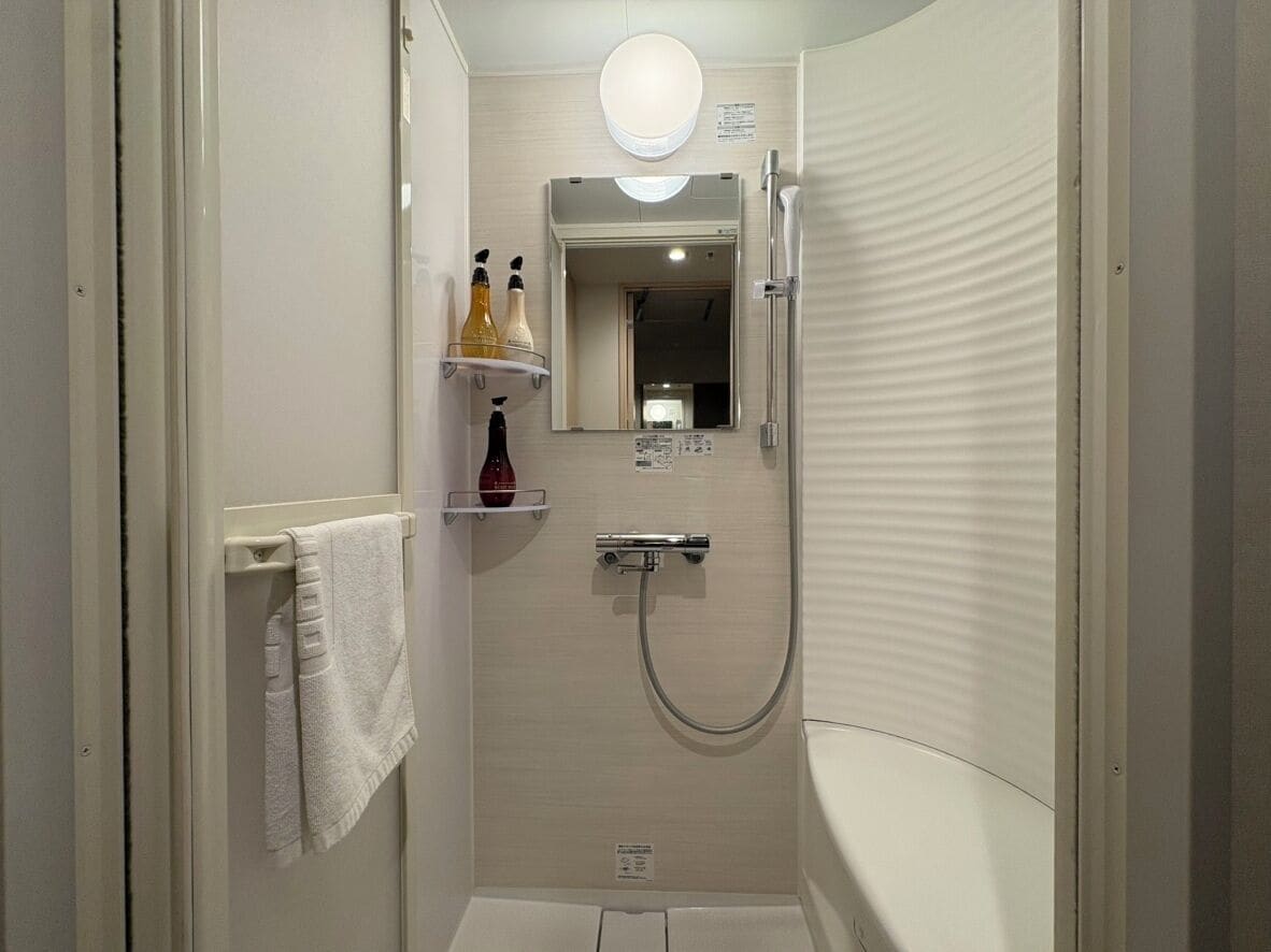 A small, enclosed bathroom with a shower, a toilet, and a mirror. There is a towel rack with a towel hanging on it.