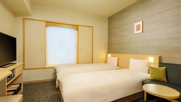 A hotel room with a bed, a television, a small table, and a window with blinds.