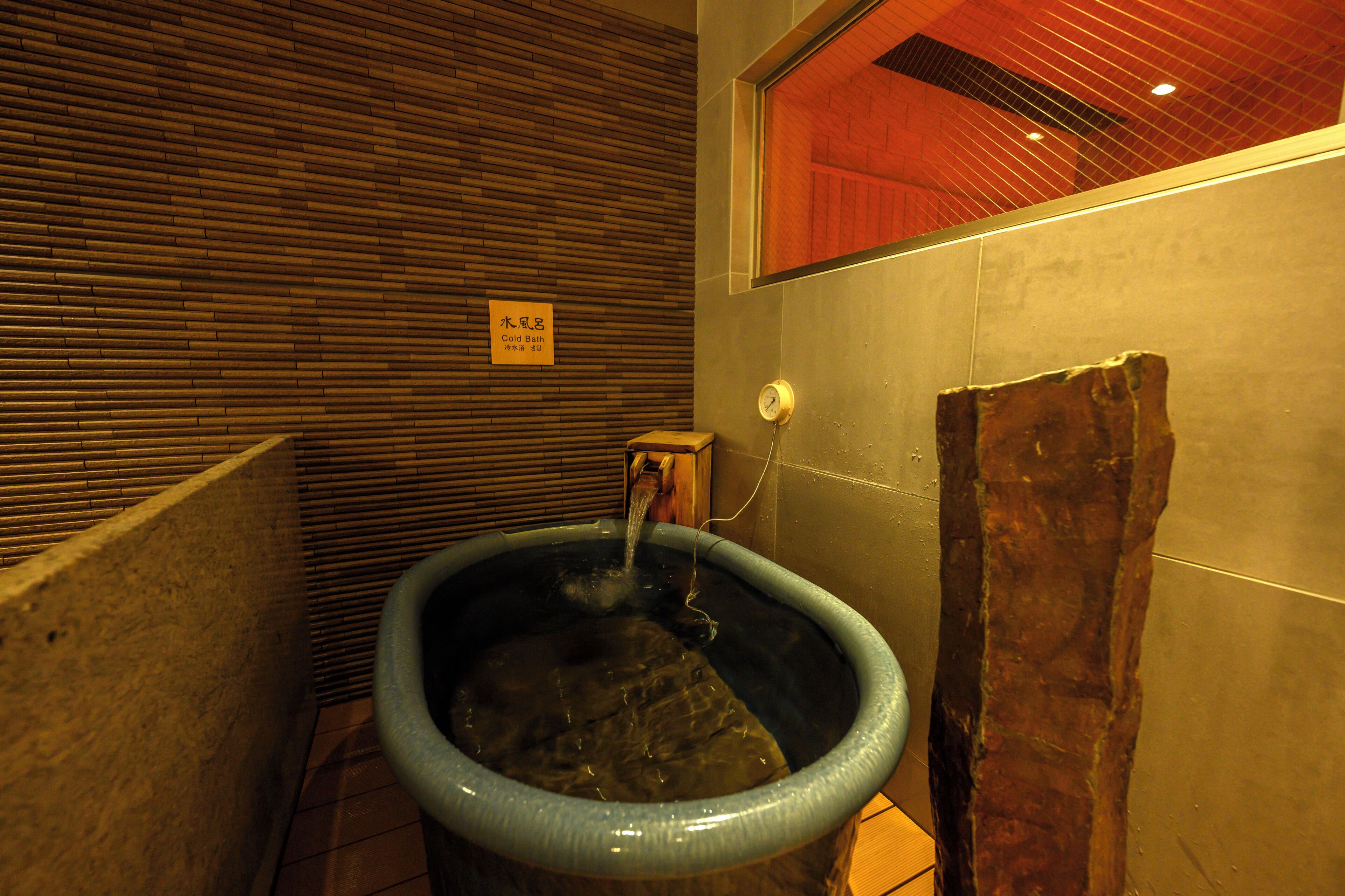 A bathroom with a large blue basin, a wooden wall, and a sign indicating a cold bath.