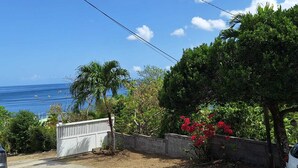 Une propriété située sur la côte, offrant une vue sur l’océan, avec un portail blanc et une végétation luxuriante.