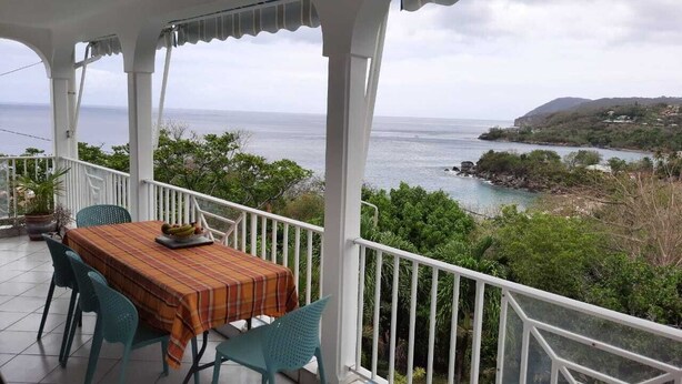 Un espace extérieur abrité, avec une table et des chaises, offrant une vue sur la côte.