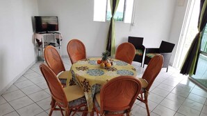 Un coin repas avec une table ronde, six chaises en osier et un téléviseur posé sur un meuble.