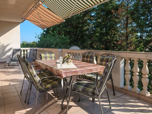 An outdoor patio with a table set for two, surrounded by metal chairs with plaid cushions.