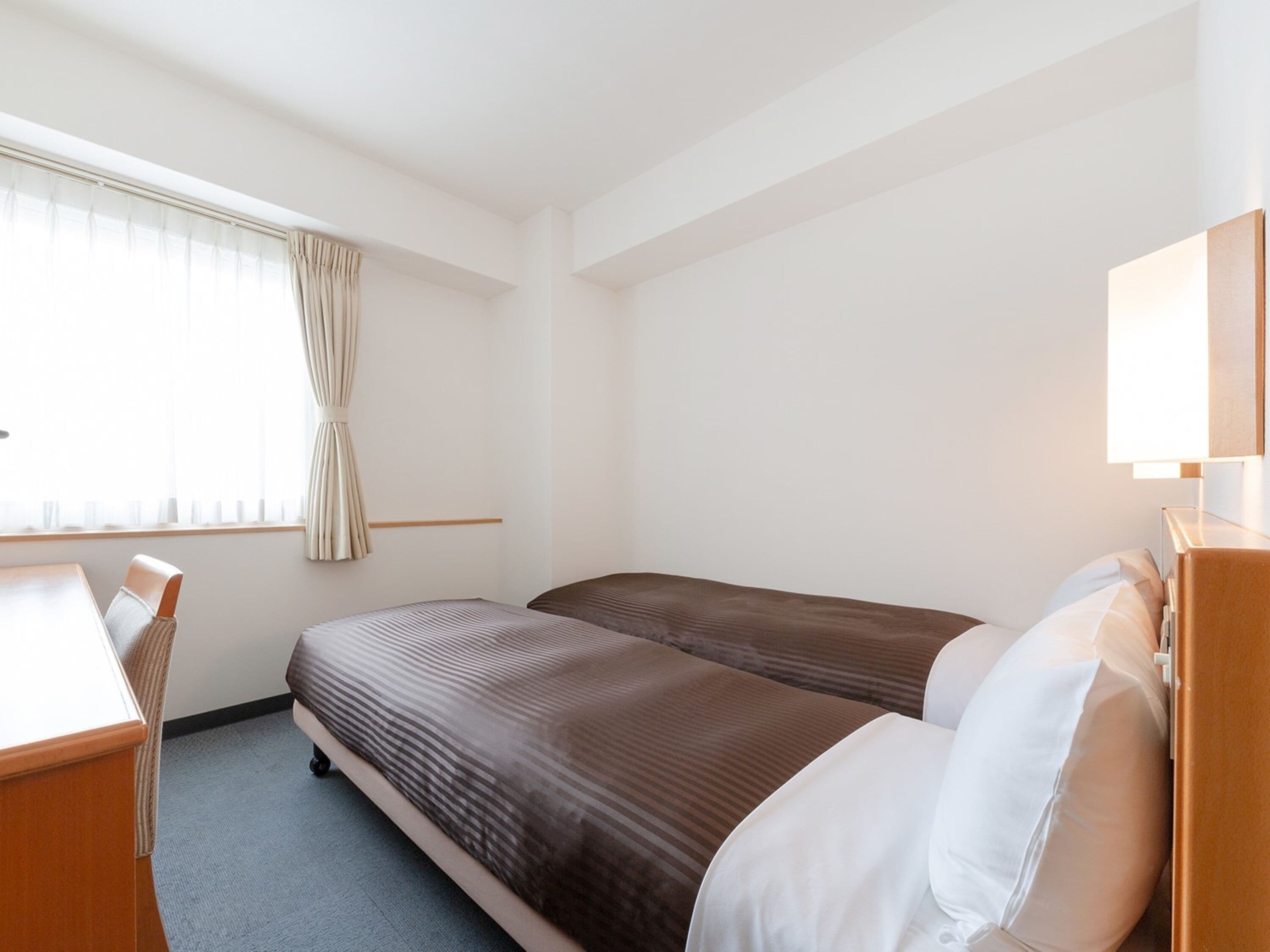 A hotel room with two single beds, a desk, and a chair.