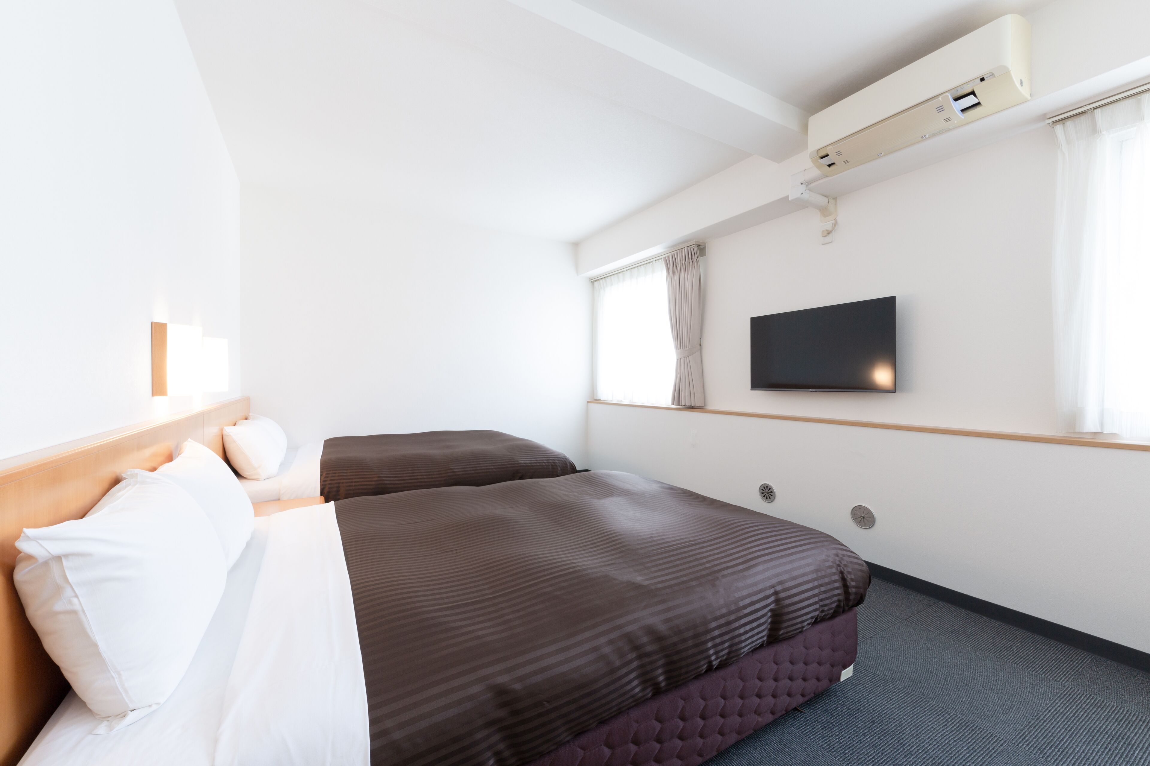 Habitación de hotel con dos camas, un televisor de pantalla plana montado en la pared y un equipo de aire acondicionado sobre las camas.
