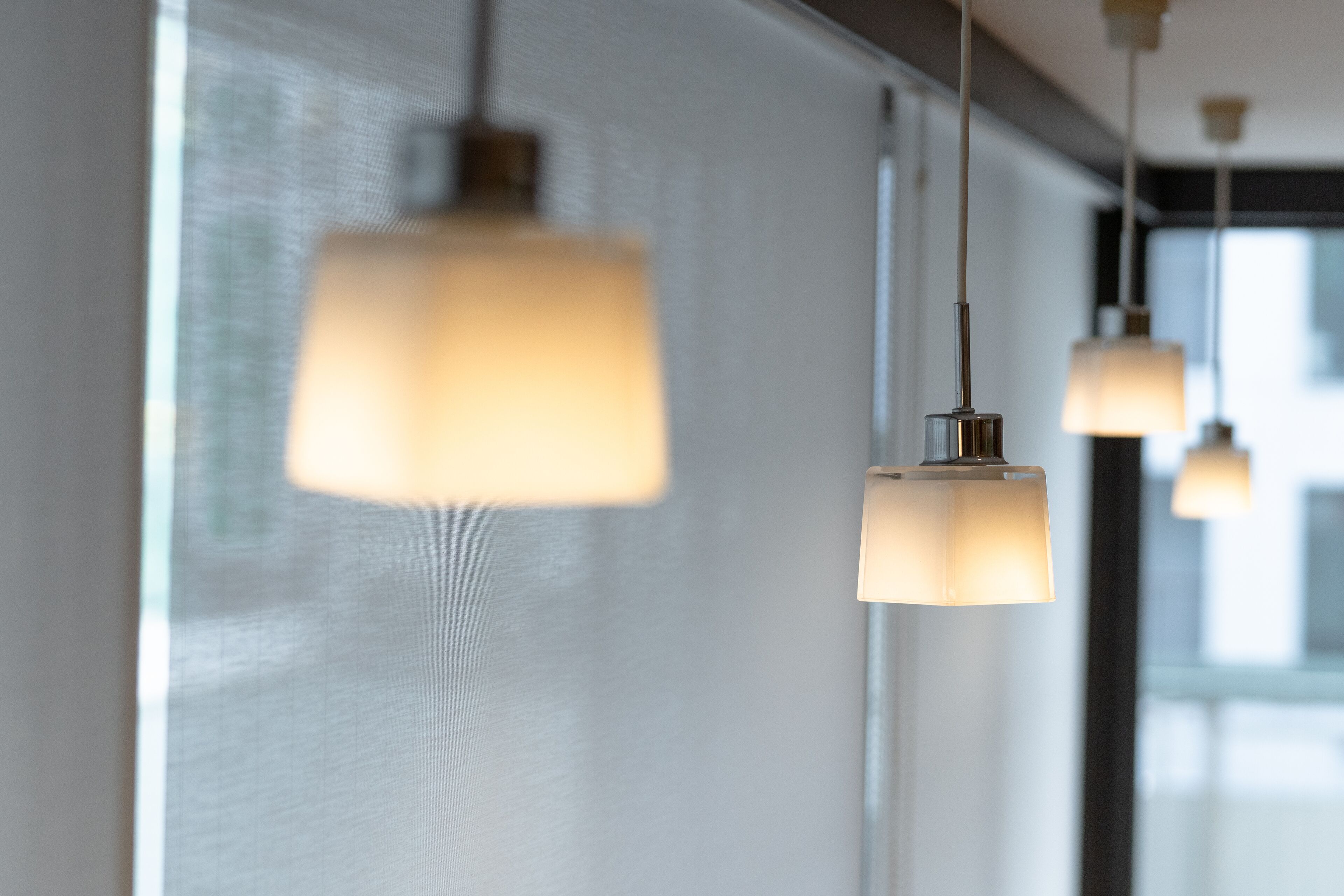 A row of pendant lights with a simple, modern design, hanging from a ceiling in a well-lit room.