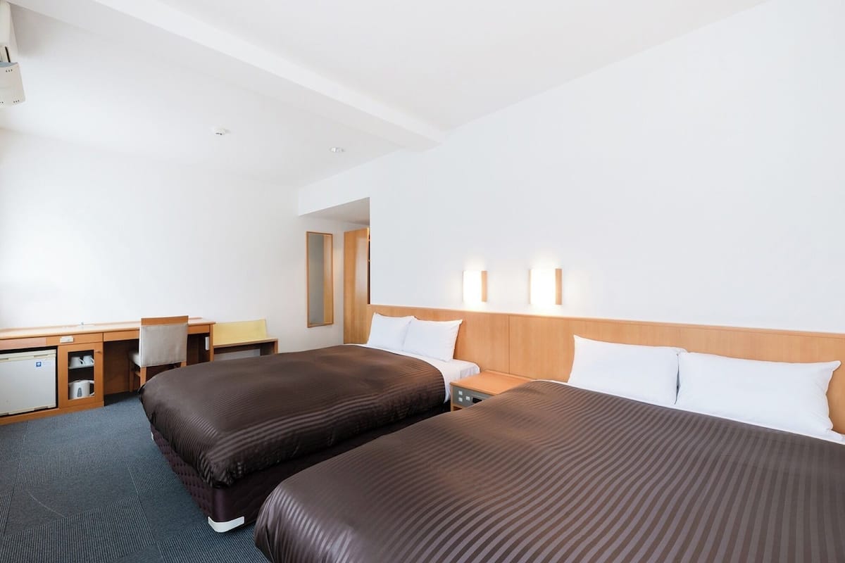 A hotel room with two beds, a desk, a chair, and a mirror.