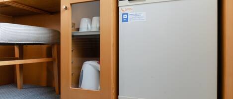 A compact kitchenette with a refrigerator, a microwave, and a small cabinet with cups and a kettle.
