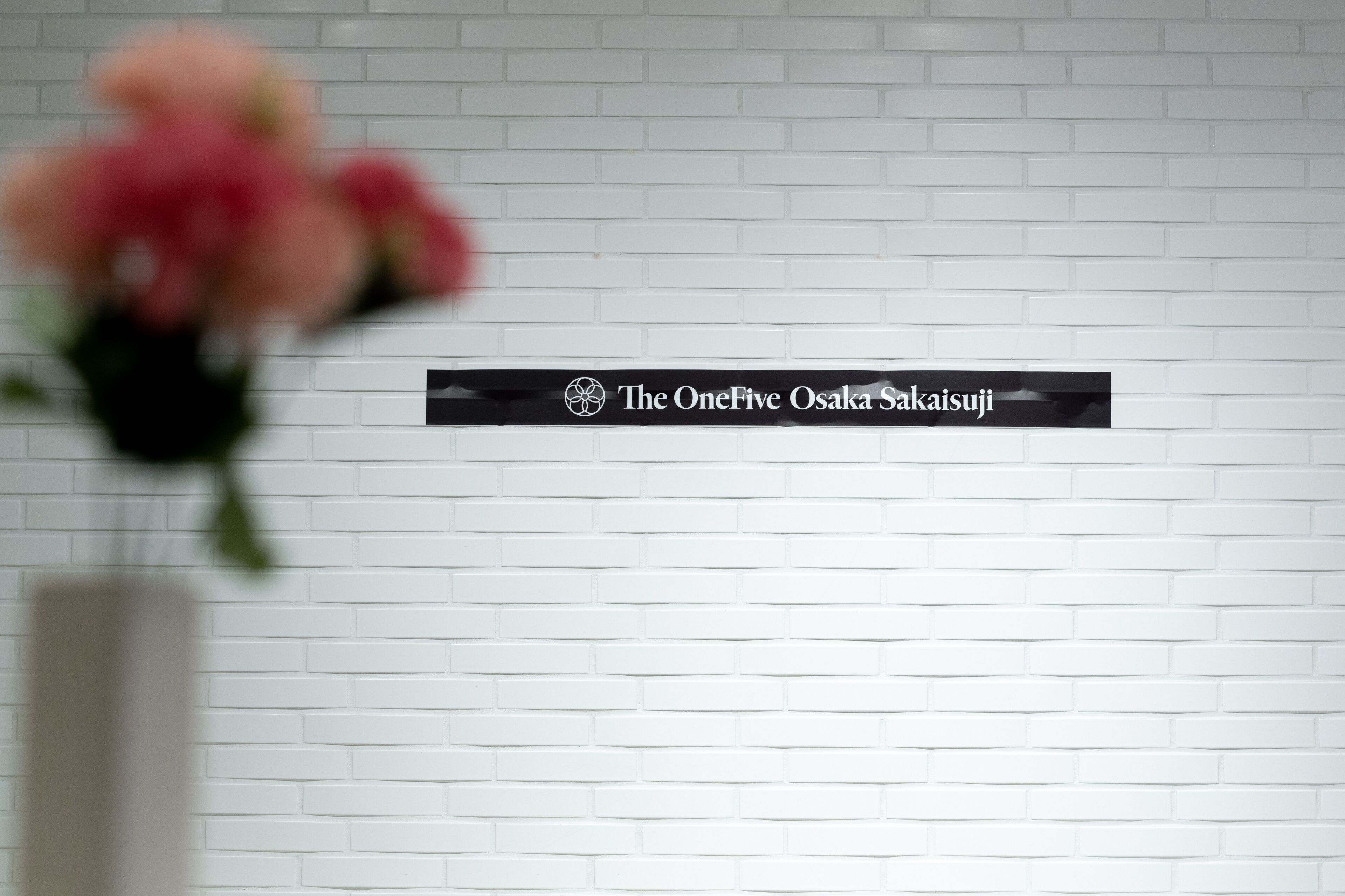 Een witte bakstenen muur met een bord waarop staat 'The OneFive Osaka Sakaiju'.