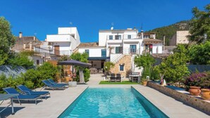 Una piscina rettangolare con lettini e una zona prendisole, circondata da edifici e vegetazione.