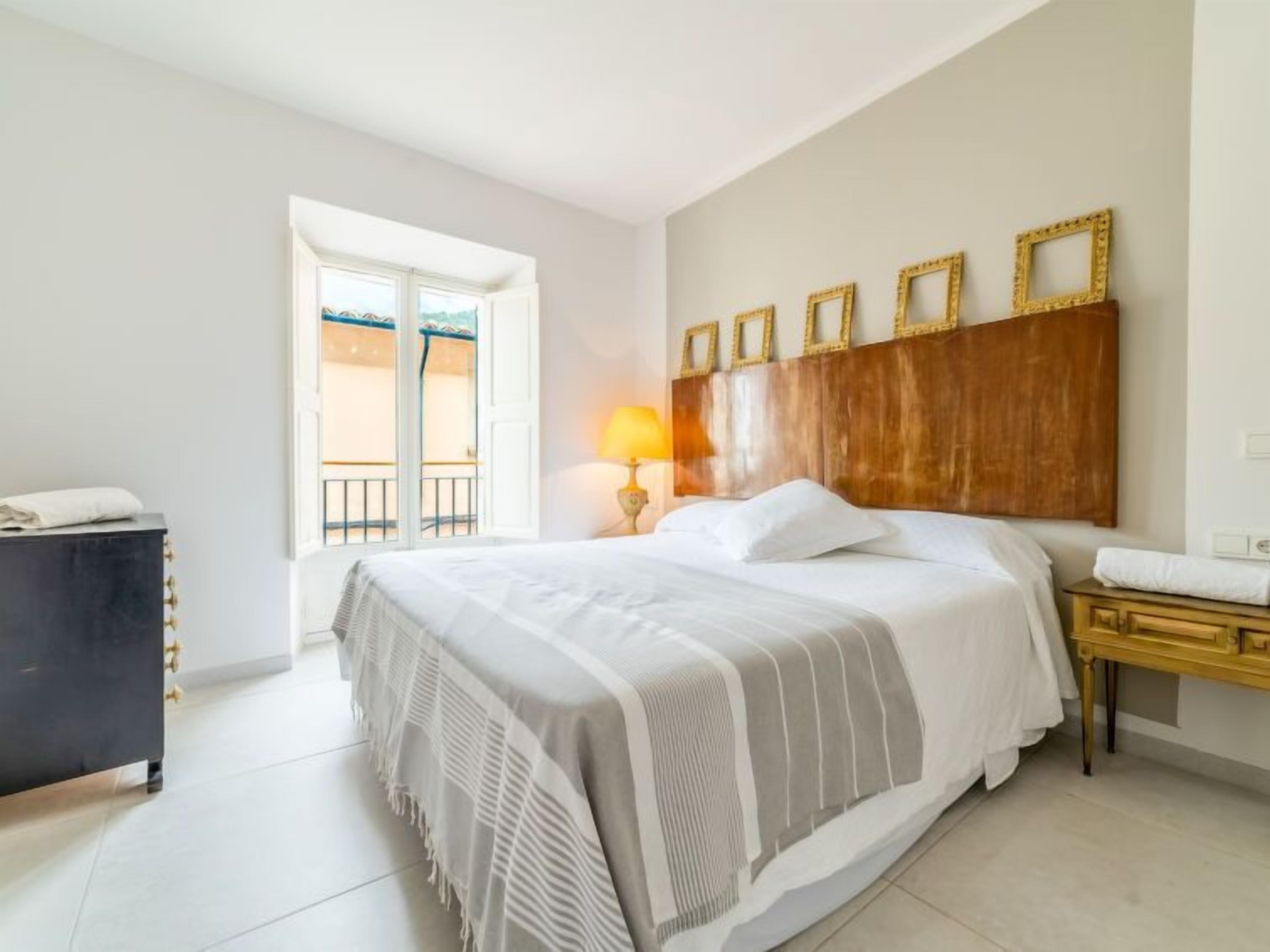 Een hotelkamer met een groot bed, een houten hoofdeinde, een nachtkastje met een lamp en een raam met uitzicht.