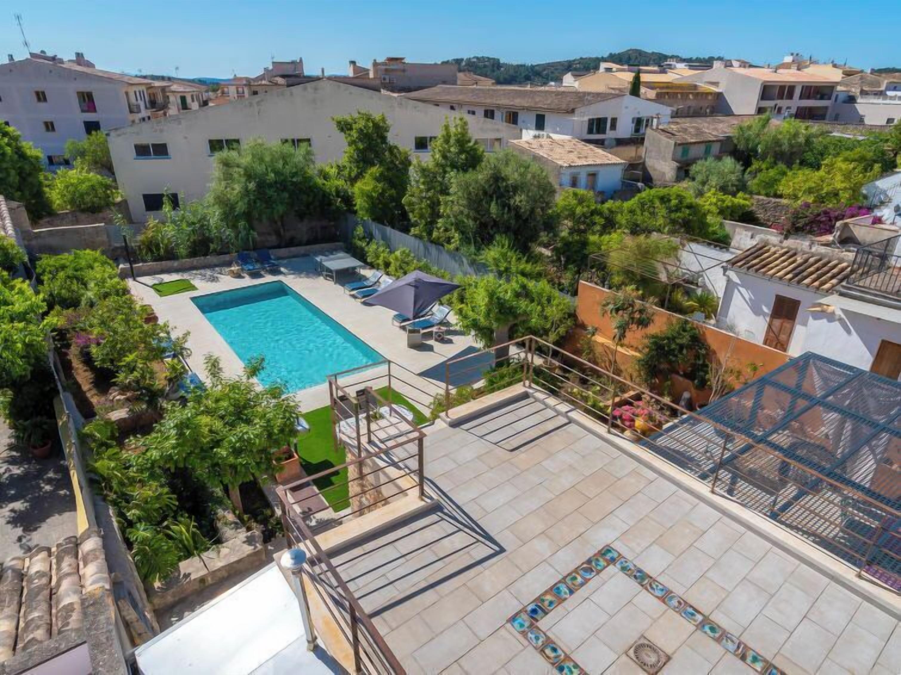 Un área de piscina en la azotea con una piscina rectangular, rodeada de vegetación y algunas sillas de descanso.