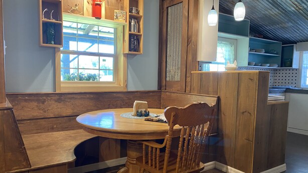 Un comedor de madera con una mesa redonda y una silla, una ventana con vistas y estantes de madera con varios objetos.