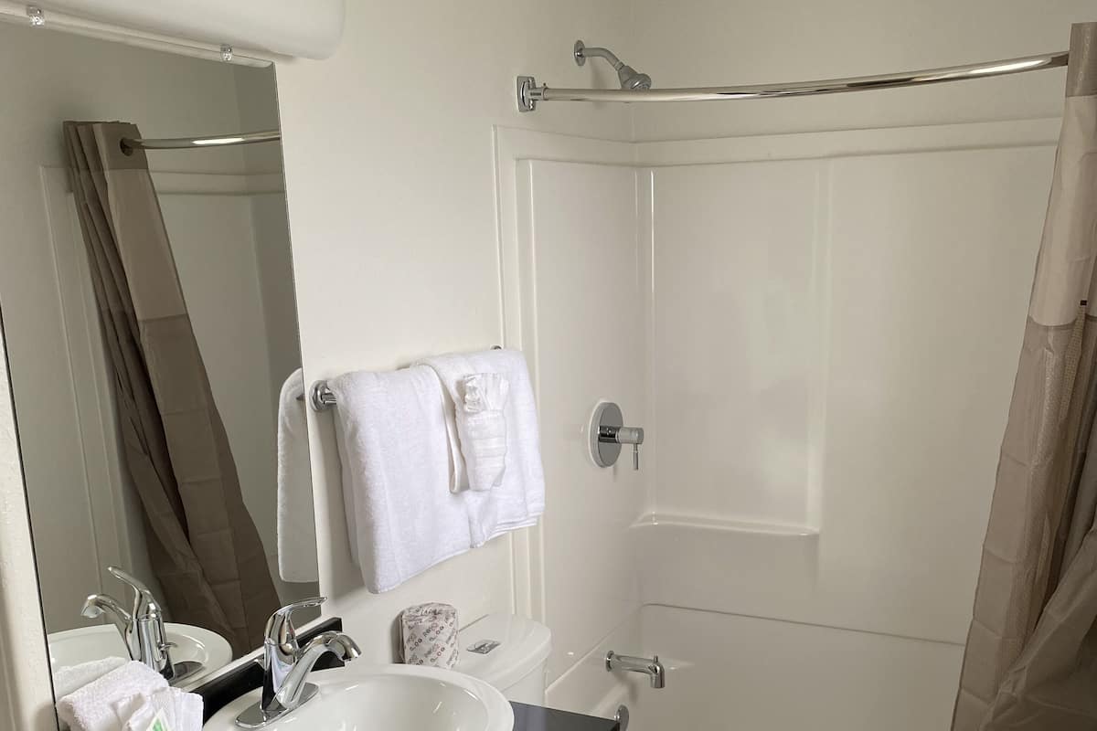 A bathroom with a white sink, mirror, and toilet, a shower curtain, and a bathtub.