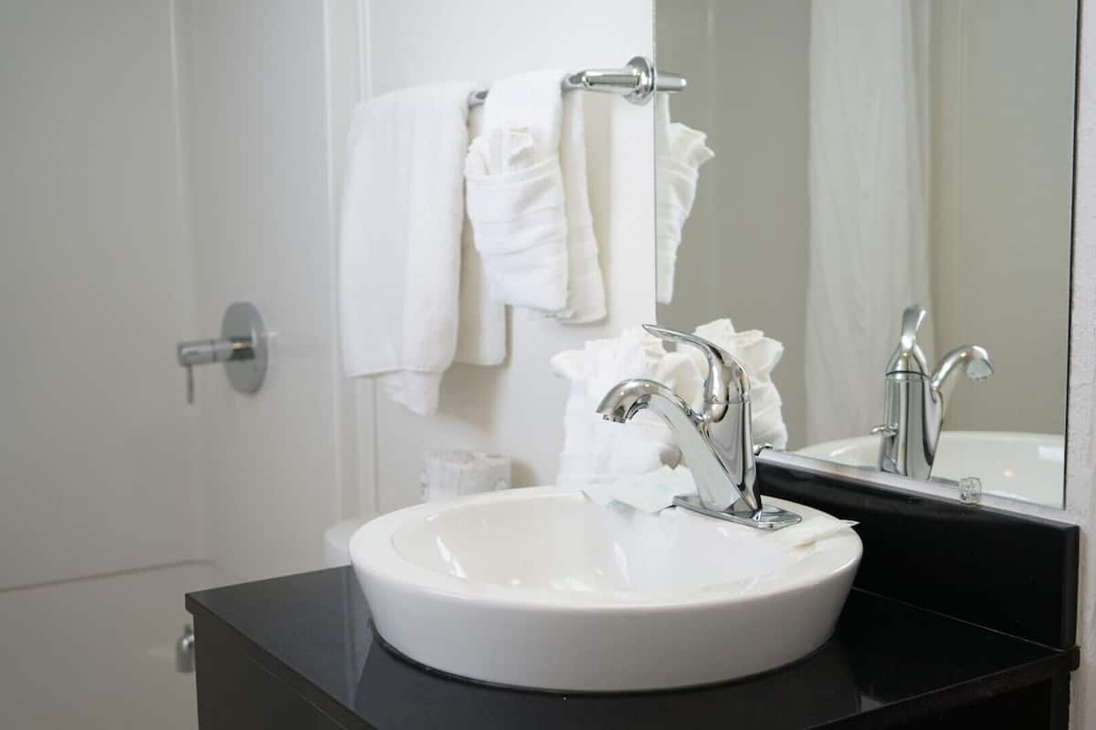A bathroom with a white sink, a black countertop, a mirror, and a towel rack with a white towel.