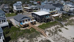 A beachfront property with a wooden deck, a covered outdoor seating area, and a sandy beach. - Charming Beachfront Cottage Awaits You! Direct access to beach off deck/walkway. (Oak Island)