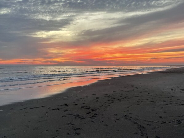 Une plage où l’on voit des empreintes de pas dans le sable, avec un coucher de soleil en arrière-plan.