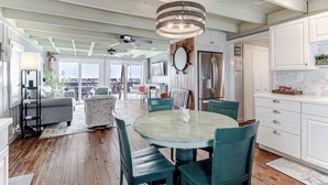 A spacious kitchen with a dining area, white cabinetry, and a large window. - Charming Beachfront Cottage Awaits You! Direct access to beach off deck/walkway. (Oak Island)