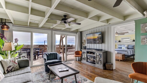 A spacious living area with a ceiling fan, a television, and a view of the outdoors. - Charming Beachfront Cottage Awaits You! Direct access to beach off deck/walkway. (Oak Island)