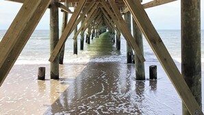 A wooden pier extending into the water with a sandy beach at the end. - Charming Beachfront Cottage Awaits You! Direct access to beach off deck/walkway. (Oak Island)
