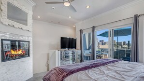 Een moderne slaapkamer met een groot bed, een open haard, een televisie en uitzicht op de stad vanaf het balkon.