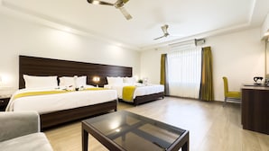 A hotel room with two beds, a glass-top table, a desk, and a ceiling fan. - The Grand Regent (Coimbatore)