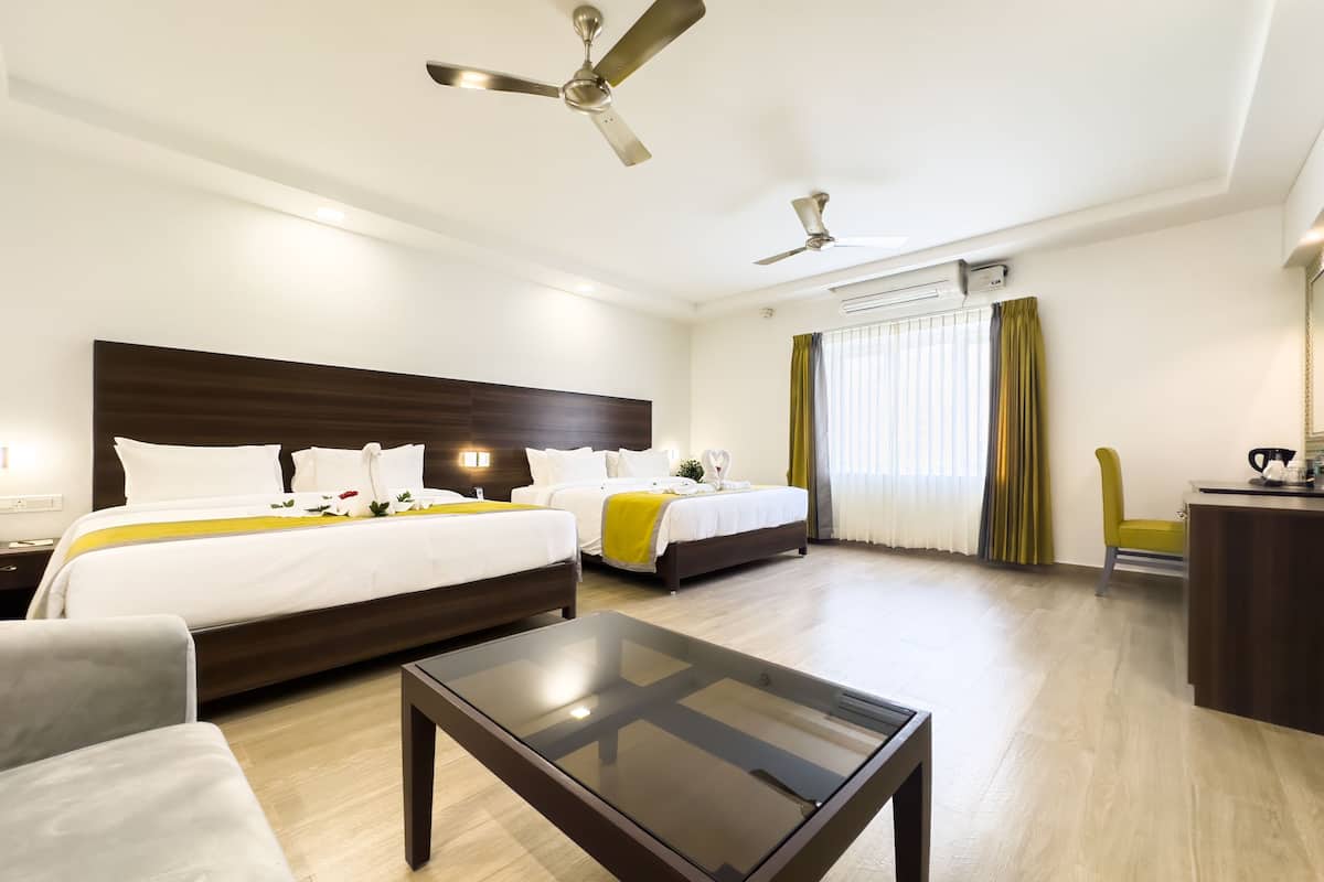 Habitación de hotel con dos camas, una mesita de vidrio, un escritorio y un ventilador de techo.