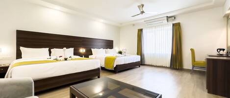A hotel room with two beds, a glass-top table, a desk, and a ceiling fan.