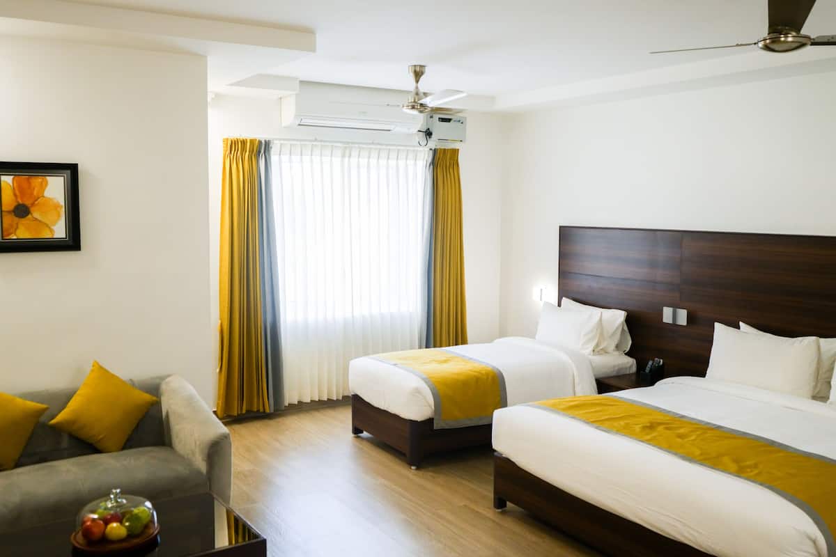 Habitación de hotel con dos camas, un sofá, una mesa de centro con fruta y un ventilador de techo.