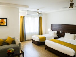 Habitación de hotel con dos camas, un sofá, una mesa de centro con fruta y un ventilador de techo.