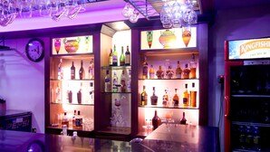 A bar area with shelves of liquor bottles, glasses, and a clock on the wall. - The Grand Regent (Coimbatore)