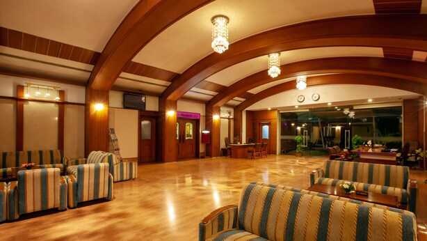 A spacious lobby with striped sofas, a wooden floor, and a chandelier. - The Grand Regent (Coimbatore)