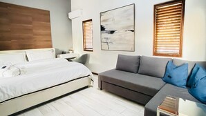 Una camera d'albergo moderna con un letto, un divano grigio, un tavolino e due finestre con tende.