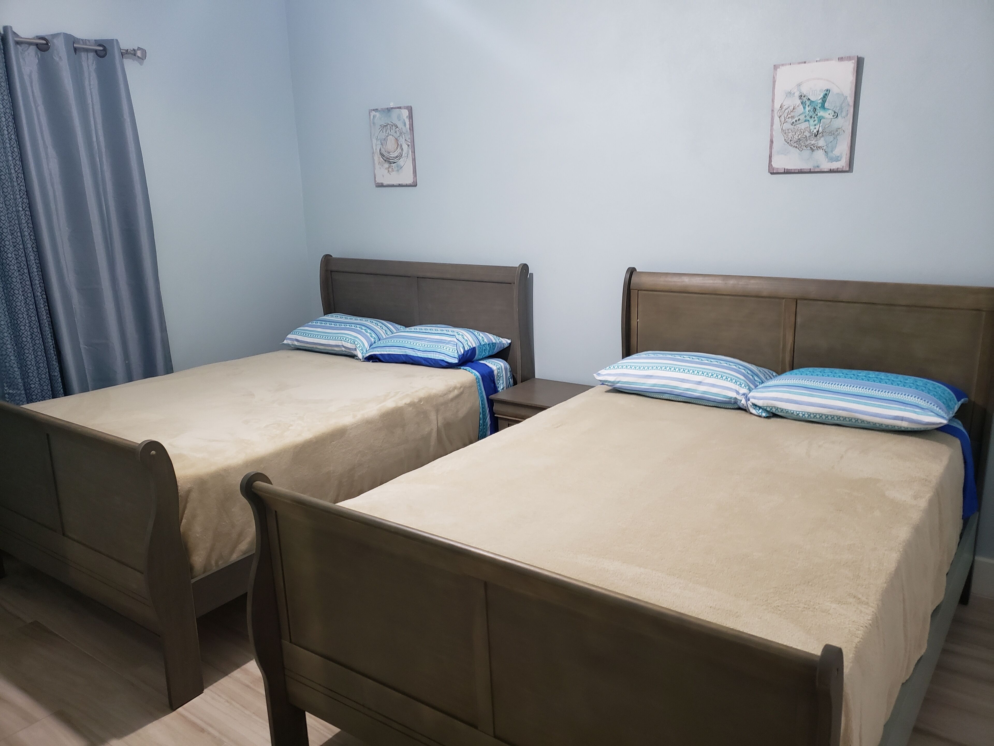 Two single beds with wooden frames and beige bedding, a small bedside table, and a wall-mounted light fixture.