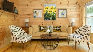 A cozy room with wooden walls, a sofa, two armchairs, a coffee table, and artwork on the walls. - “Just BEE🐝Log Cabin"-Stunning, peaceful, NEW, -10 min to Dwtn Asheville, dogs ok (Asheville)