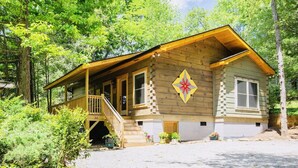 A wooden cabin with a porch, a staircase, and a decorative diamond-shaped sign on the wall. - “Just BEE🐝Log Cabin"-Stunning, peaceful, NEW, -10 min to Dwtn Asheville, dogs ok (Asheville)