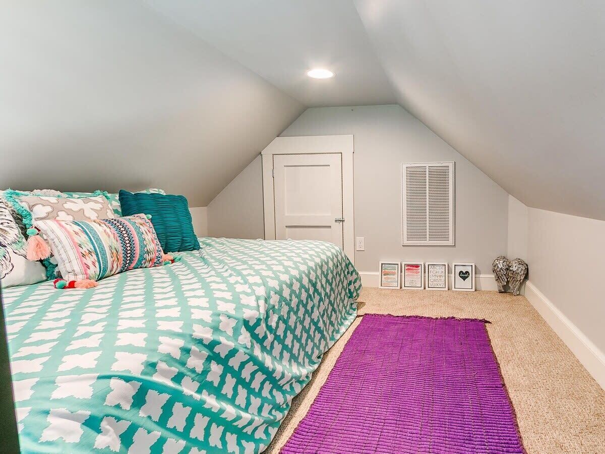 Ein Schlafzimmer mit einem Bett, einem violetten Teppich, einer weißen Tür und einem Fenster mit Fensterläden.