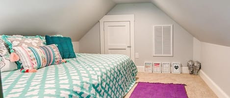 Ein Schlafzimmer mit einem Bett, einem violetten Teppich, einer weißen Tür und einem Fenster mit Fensterläden.