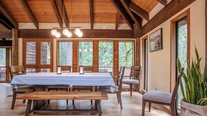 A wooden dining area with a table set for four, large windows, and a ceiling with exposed beams.