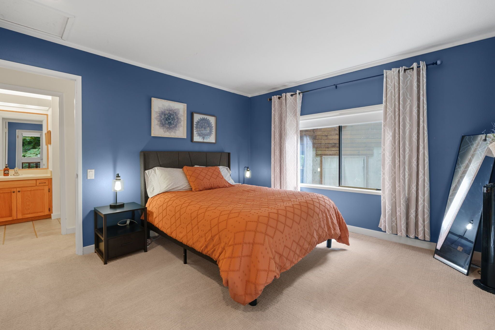 A bedroom with a bed, bedside table, lamp, and a window with curtains.
