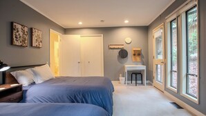 A bedroom with two beds, a desk, and a large window.