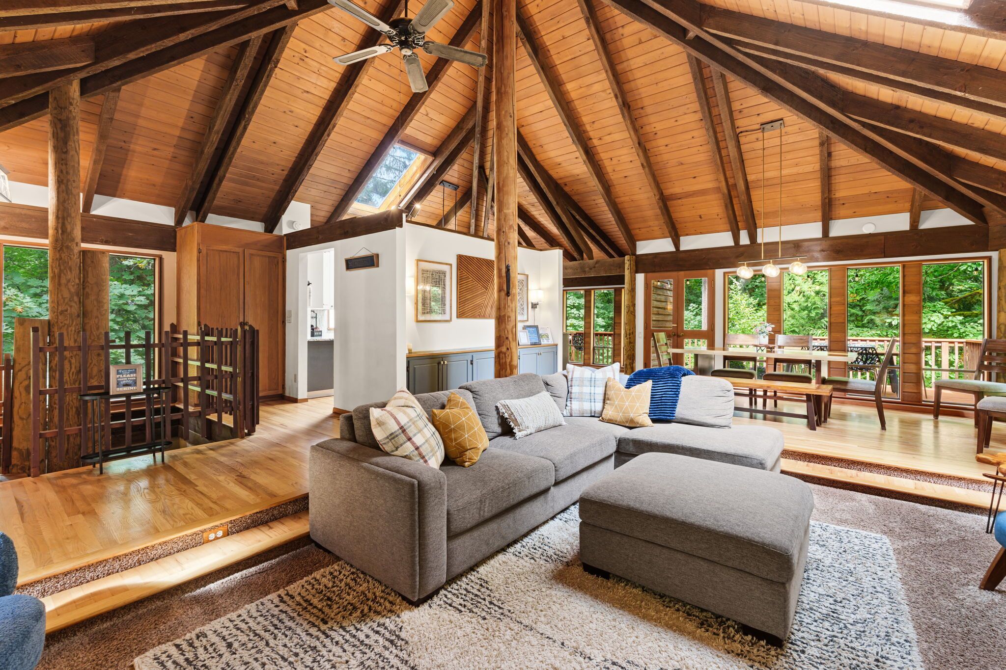 A spacious living room with a high ceiling, wooden beams, a large sofa, and a dining area with natural light.