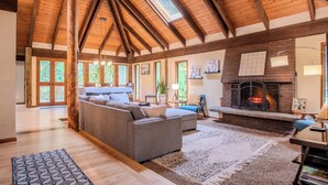 A spacious living room with a high wooden ceiling, a fireplace, and a large sofa.