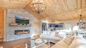 Ein geräumiges Wohnzimmer mit Kamin, Holzboden und einer modernen Küche im Hintergrund.
