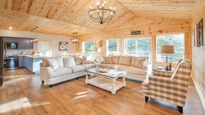 Ein geräumiger Wohnbereich mit Holzboden, einem großen Sofa, einem Couchtisch und einem karierten Sessel.