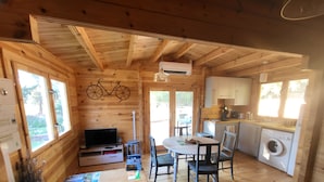 A cozy cabin with wooden walls and ceilings, a dining area with a table and chairs, a kitchen with a washing machine, and a television in the living area. - Le Colibri dans la colline rated 3*. (La Ciotat)