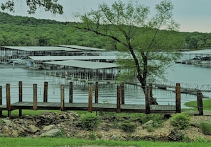 A lakeside property with multiple docked boats, a wooden deck, and a forested hillside in the background. - Lighthouse 5B (Kimberling City)
