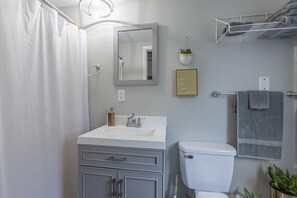 A bathroom with a white sink, mirror, and toilet. There are two plants, a towel rack, and a sign on the wall. - Lighthouse 5B (Kimberling City)