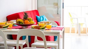 A dining area with a table set for breakfast, featuring a fruit bowl, plates, and glasses of orange juice. - 1.1 Beautiful seafront with balcony and WIFI (Arona)
