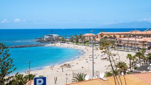 A coastal hotel with a beach view, a parking sign, and a clear blue sky. - 1.1 Beautiful seafront with balcony and WIFI (Arona)